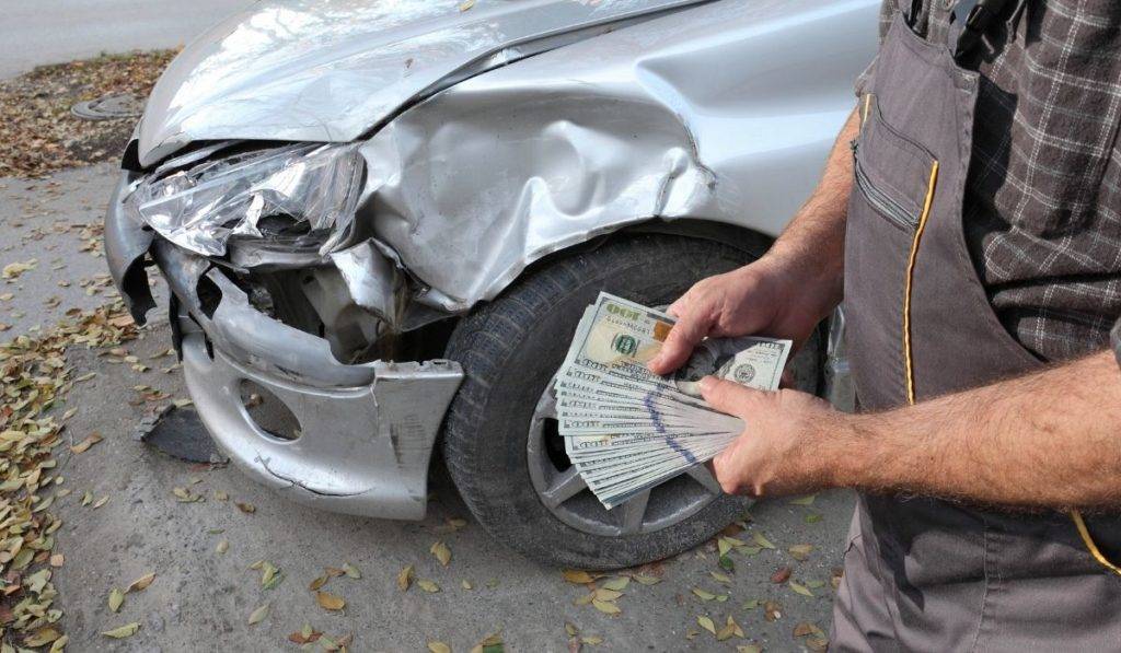 man holding cash next to damaged car