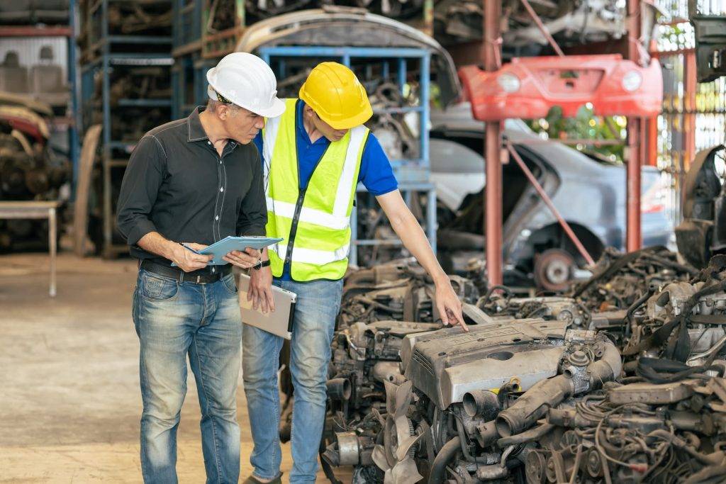 Two workers looking at car scrap parts in a Swansea yard